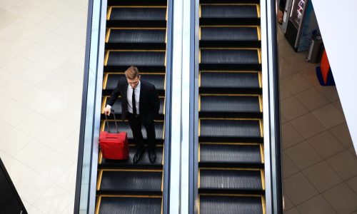 Business man going down escalator holding travel bag